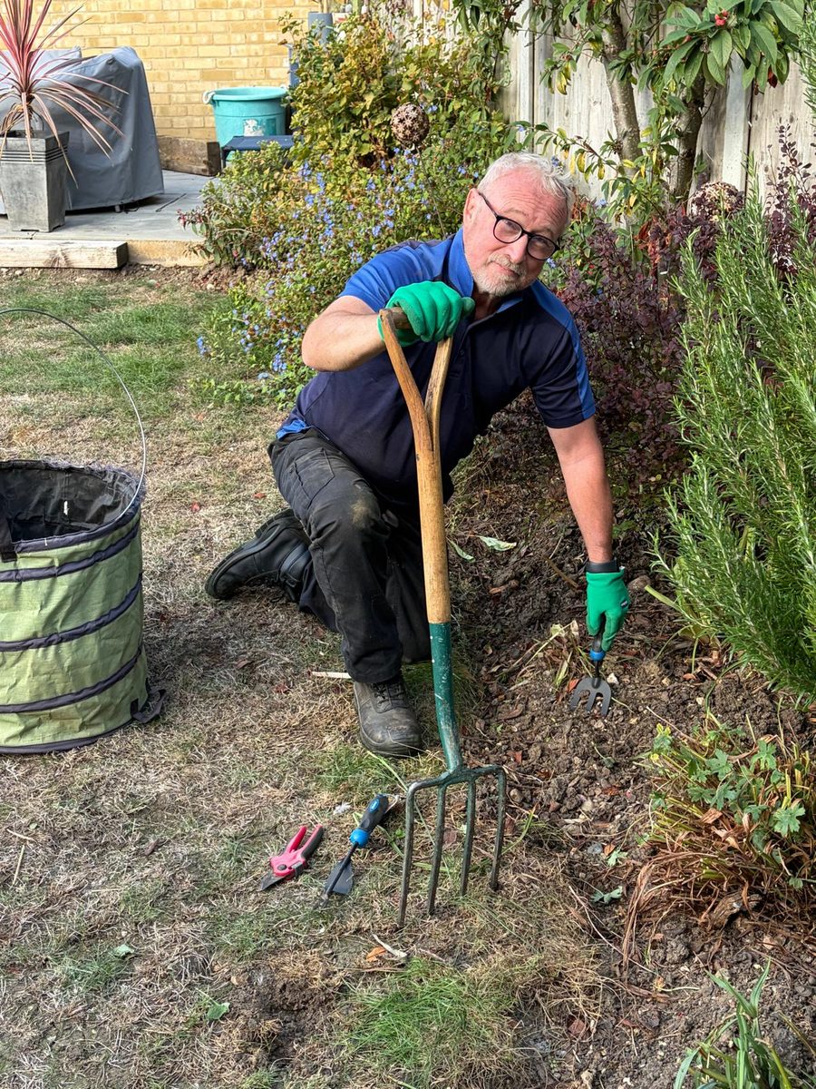 Paul, a full-time professional gardener, kneeling to weed a garden border with a hand fork and tools